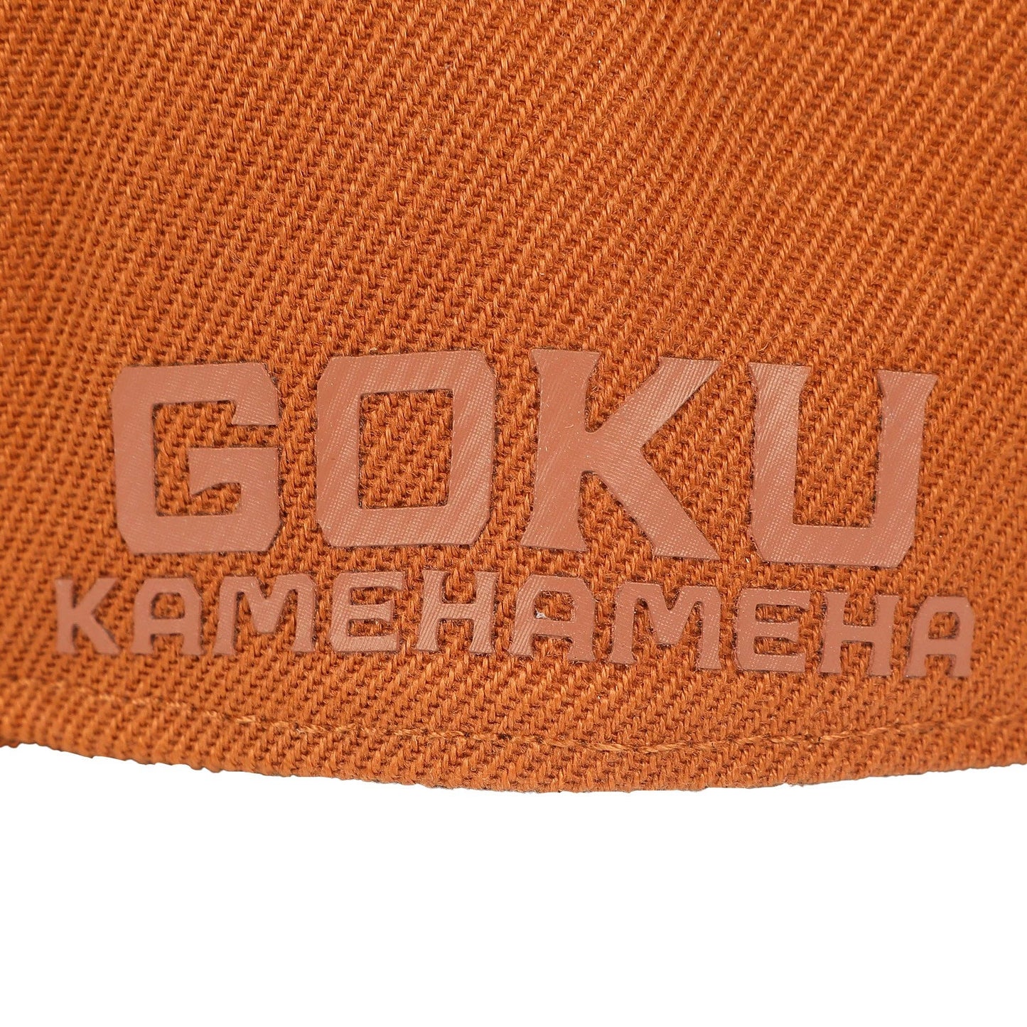 Close-up of an orange woven fabric surface with embossed text reading 'GOKU' and 'KAMEHAMEHA' in a matching orange-brown tone, with a white background visible at the bottom.