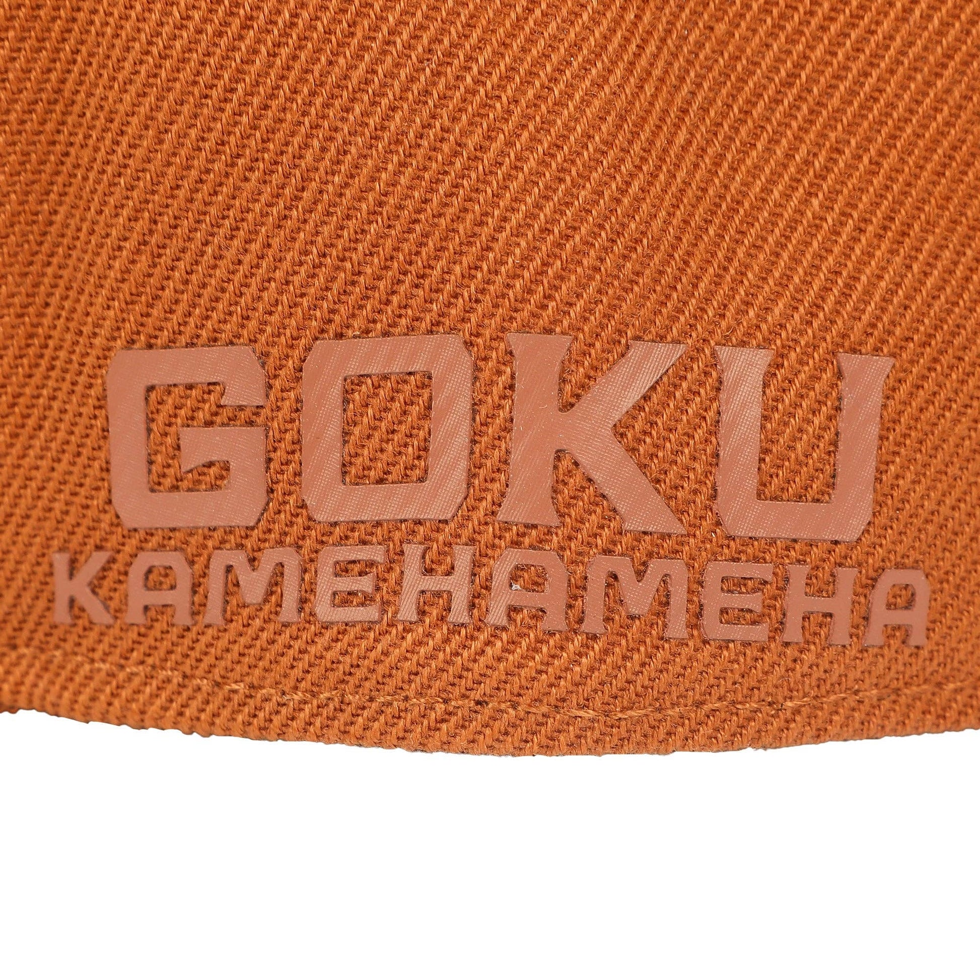 Close-up of an orange woven fabric surface with embossed text reading 'GOKU' and 'KAMEHAMEHA' in a matching orange-brown tone, with a white background visible at the bottom.