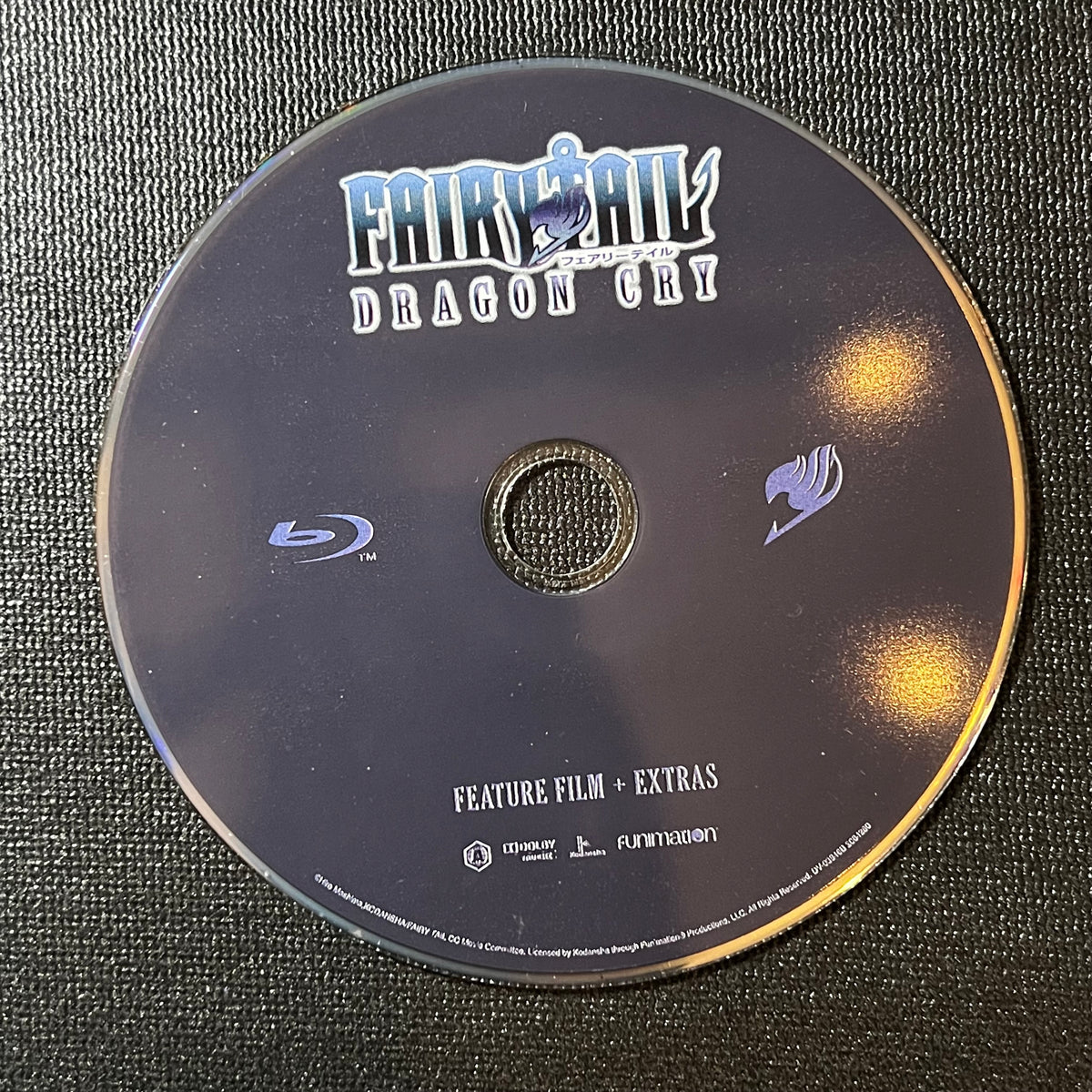 Blu-ray disc with 'Fairy Tail' branding on a textured surface