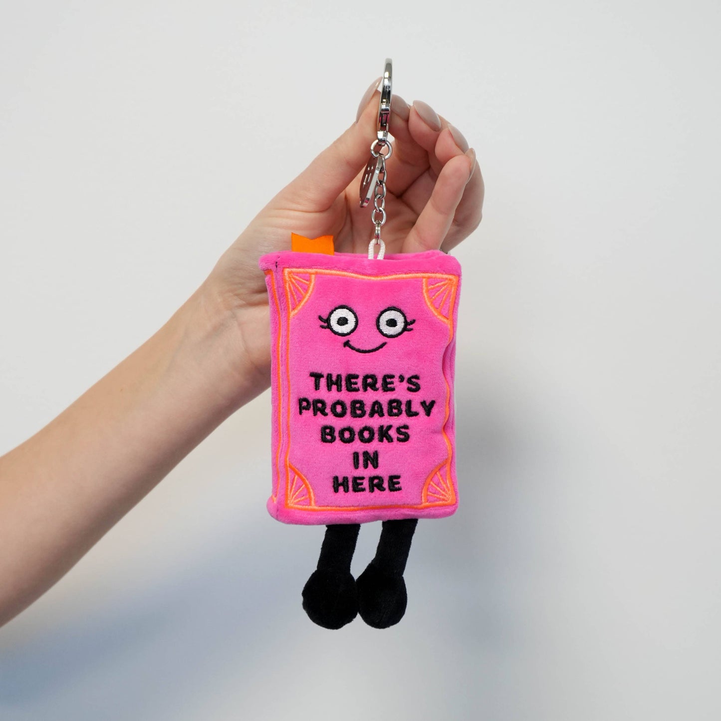 Plush keychain shaped like a book with text held by a hand against a plain background
